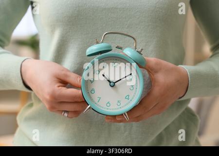Woman setting time on alarm clock at home, closeup. Daylight saving time concept Stock Photo