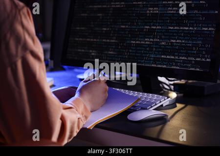 Female programmer working with notebook and computer in dark office at night, closeup Stock Photo