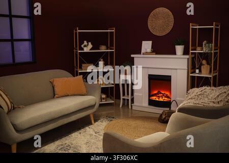 Cozy living room interior with a lit electric fireplace, comfortable sofa, and decorative shelves at night Stock Photo