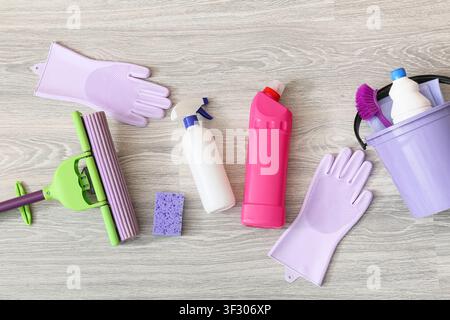 Household cleaning supplies and equipment including a mop, gloves, sponge, and bottles of detergent on a wooden floor Stock Photo