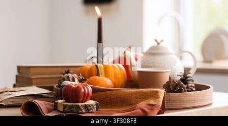 Autumnal table setting with lit pumpkin candles, small gourds, pinecones, and books for cozy fall decor Stock Photo