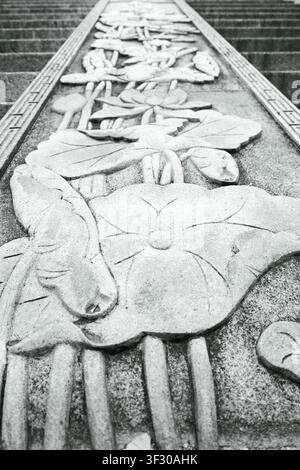 Black and white close view of a stone flower carving on outdoor steps, showing texture, pattern, and depth in a calm architectural scene. Stock Photo