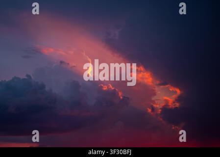 Dramatic sky revealing atmospheric clouds at twilight, showing glowing orange and purple hues with a bright sunray piercing through the dark cloud formations during a beautiful sunset Stock Photo