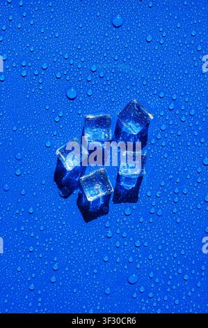 Clear ice cubes arranged on a wet, vibrant blue surface with water droplets. Stock Photo