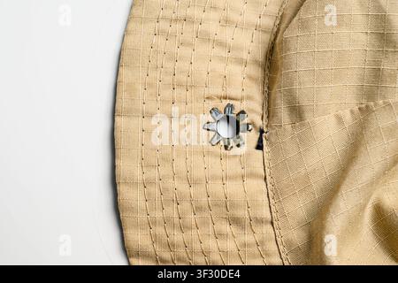 Macro shot of a tan boonie hat's brim and crown, featuring durable ripstop fabric, parallel stitching, and a star-shaped metal ventilation eyelet on a Stock Photo