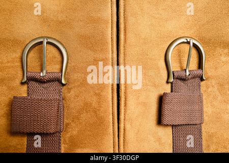 Detailed close-up featuring two rustic brass buckles with brown canvas straps on a tan suede surface with a central vertical seam, highlighting textur Stock Photo