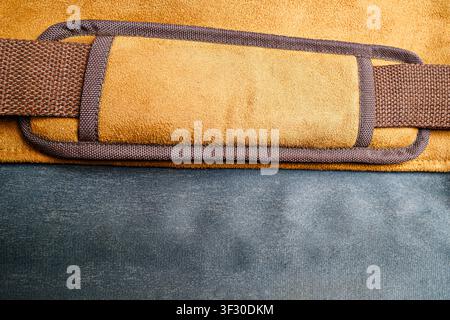 Macro view of a tan suede shoulder strap with a brown woven belt on a blue canvas fabric background. High-quality details showing material stitching, Stock Photo