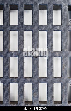 Detailed shot of a textured dark grey plastic ventilation grid with rectangular openings. The surface has a fine pattern and some dust, showing geomet Stock Photo