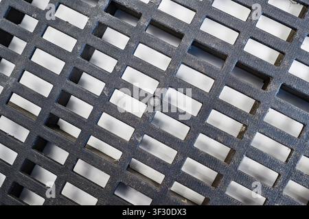 Detailed shot of a textured dark grey plastic ventilation grid with rectangular openings. The surface has a fine pattern and some dust, showing geomet Stock Photo