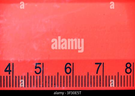 Detailed macro view of a bright red plastic ruler with black markings and numbers from four to eight. Useful for themes like back to school, math, eng Stock Photo