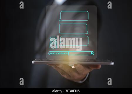 A businessman holds a tablet showcasing a futuristic holographic AI chatbot interface with speech bubbles and a message bar, representing automated cu Stock Photo