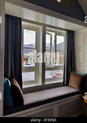 Siglufjörður's harbor view from the hotel window, snow mountain, sea, fishing boats under a clear blue sky, Northern Iceland Stock Photo