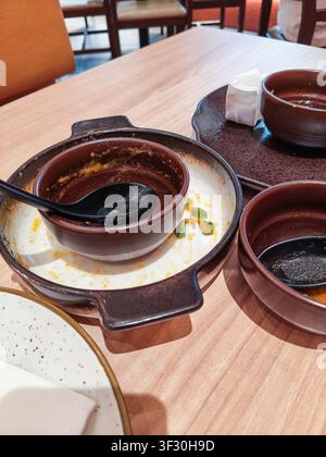 Dirty dishes, empty sauce bowls, and black spoons left on a wooden restaurant table after a delicious meal, showing leftovers and food stains. Stock Photo