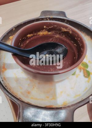 Dirty dishes, empty sauce bowls, and black spoons left on a wooden restaurant table after a delicious meal, showing leftovers and food stains. Stock Photo