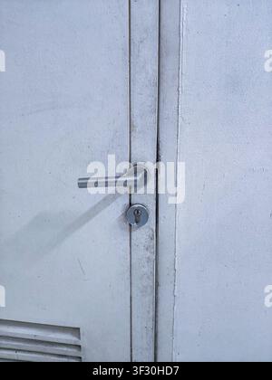 A modern stainless steel lever door handle with keyhole mounted on a white wooden door, featuring a simple and functional architectural design. Stock Photo