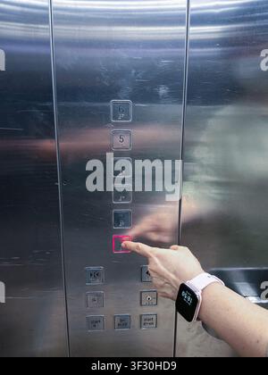Hand pressing a lit button on a metallic elevator control panel with braille numbers, selecting a floor inside a modern building lift. Stock Photo