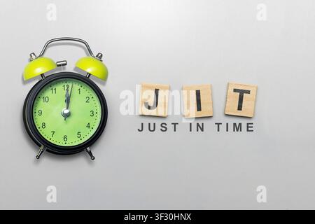 Conceptual flat lay representing Just In Time (JIT) management with a green alarm clock and wooden tiles. Ideal for logistics, business efficiency, an Stock Photo