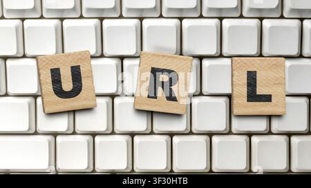 The word URL spelled out using wooden alphabet tiles resting on a vintage white computer keyboard, representing web addresses, internet navigation, an Stock Photo