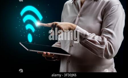 Person holding a tablet and pointing to a glowing blue Wi-Fi symbol representing high-speed internet, wireless connectivity, and digital technology ne Stock Photo