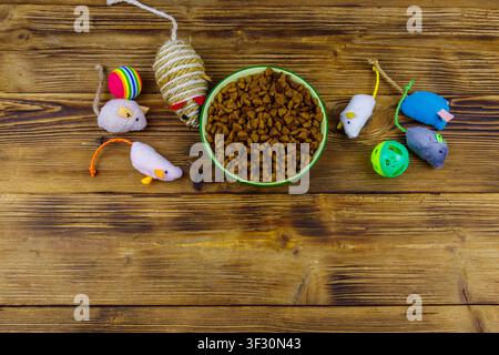 Set of toys for cat and bowl with dry pet food on wooden background. Top view. Pet care concept Stock Photo