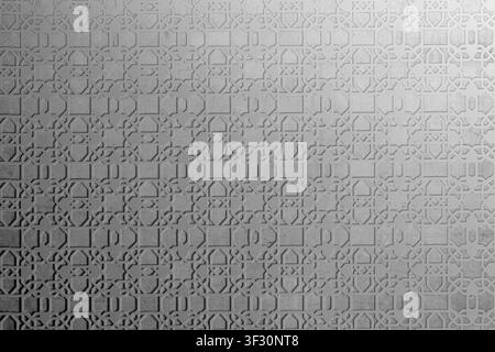 A sophisticated grey wall featuring an intricate Islamic geometric fretwork pattern. Side lighting enhances the texture and depth of the architectural Stock Photo