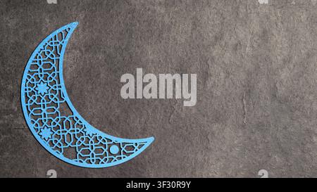 A decorative blue glittery crescent moon featuring an intricate geometric pattern, placed on a dark textured stone background. Ideal for Ramadan, Eid, Stock Photo