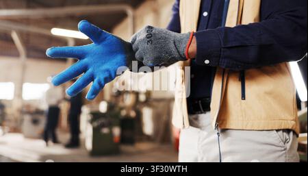 Hands, gloves and worker in workshop for carpentry, labor and PPE with preparing for woodworking. Carpenter person, protective gear and ready for Stock Photo