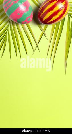 A flat lay composition featuring two colorful hand-painted Easter eggs and green palm leaves over a bright neon yellow-green background with ample cop Stock Photo