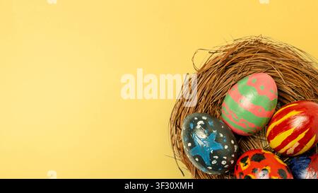 Top-down view of uniquely hand-painted Easter eggs in a bird's nest on a vibrant yellow background. Perfect for holiday greetings and spring celebrati Stock Photo