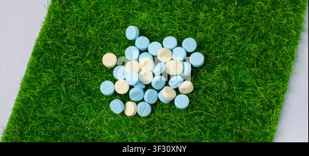 White and blue pills arranged in a pile on a green grass mat over white background, suitable for medicine, pharmacy, supplement, healthcare Stock Photo
