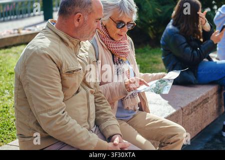 older couple sitting, woman holding a map and pointing, discussing directions or a location with the man next to her. A moment of travel, planning Stock Photo