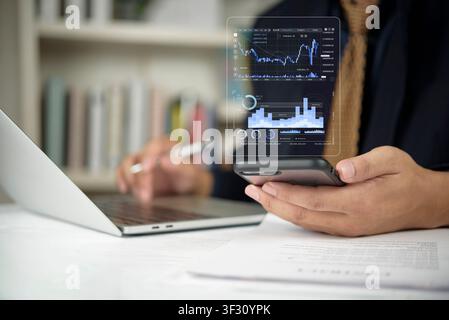 Businessman using laptop and smartphone with virtual stock market chart hologram. mobile financial trading, forex investment application, fintech data Stock Photo