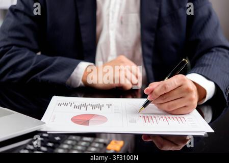 businessman hands in suit holding pen and analyzing financial data, pie chart and bar graph on desk. Corporate accounting, business investment, market Stock Photo