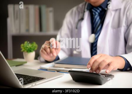 doctor using calculator and laptop for medical cost calculation, health insurance billing, and hospital budget management in clinic office. High quali Stock Photo