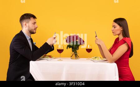 Couple Using Cellphones Sitting At Table Posing Over Yellow Background Stock Photo