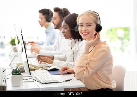 Team of diverse hotline operators with headphones providing service to clients at call center Stock Photo