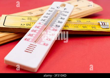 Close Up Foreground View of White Plastic Thermometer Over Wooden Thermometers on Red Background Stock Photo