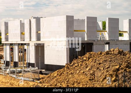 Construction process underway with concrete block walls being erected on building site. Heavy machinery and earthworks visible in foreground, indicating active development.  Stock Photo