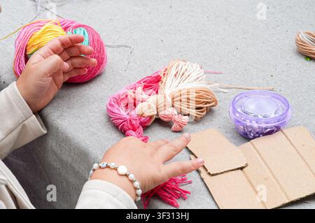 Close-up of children's hands making a craft with colorful yarn. Making a motanka doll Stock Photo