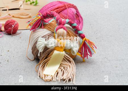 doll made of multi-colored yarn and a ball of yarn on a gray background. Threads for knitting. Handmade products Stock Photo