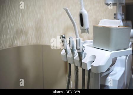 A close-up view of professional dental handpieces, a suction tool, and a tissue box on a white instrument tray in a clean, modern dentist office setti Stock Photo