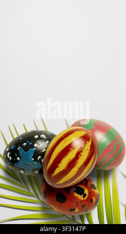 A vertical high-angle shot of four uniquely hand-painted Easter eggs resting on green palm leaves against a clean white background with ample copy spa Stock Photo