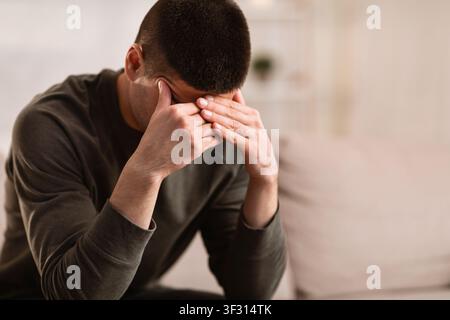 Ill man sitting on sofa with head on his hands Stock Photo
