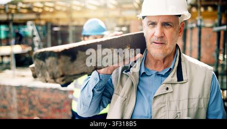 Thinking, man and construction worker with plank on site for ideas on building, renovation or repairs. Wood beam, planning and mature civil engineer Stock Photo