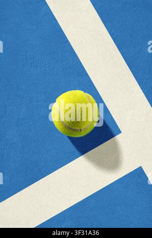Overhead view of a yellow tennis ball on a textured blue synthetic court at the intersection of white boundary lines, featuring a distinct shadow unde Stock Photo
