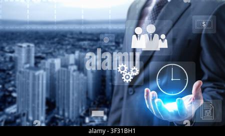 Businessman holding glowing digital icons for time management, teamwork, and processes against a blurred urban background, representing efficient busi Stock Photo