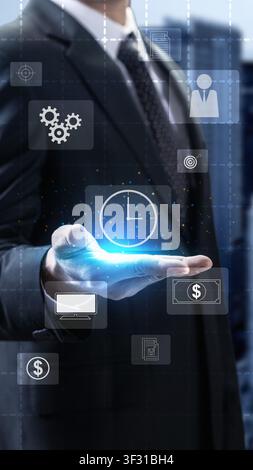 Businessman holding glowing digital icons for time management, teamwork, and processes against a blurred urban background, representing efficient busi Stock Photo