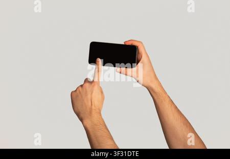 Unrecognizable millennial man touching screen of cellphone over light background, space for mobile app design Stock Photo