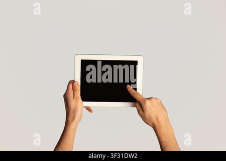 Unrecognizable man touching screen of modern tablet computer on light background, mockup for design Stock Photo