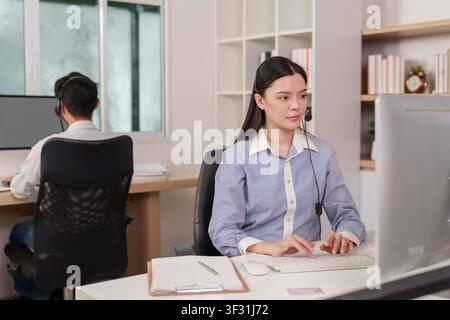 Asian call center agents with headsets working at computers in modern office Stock Photo